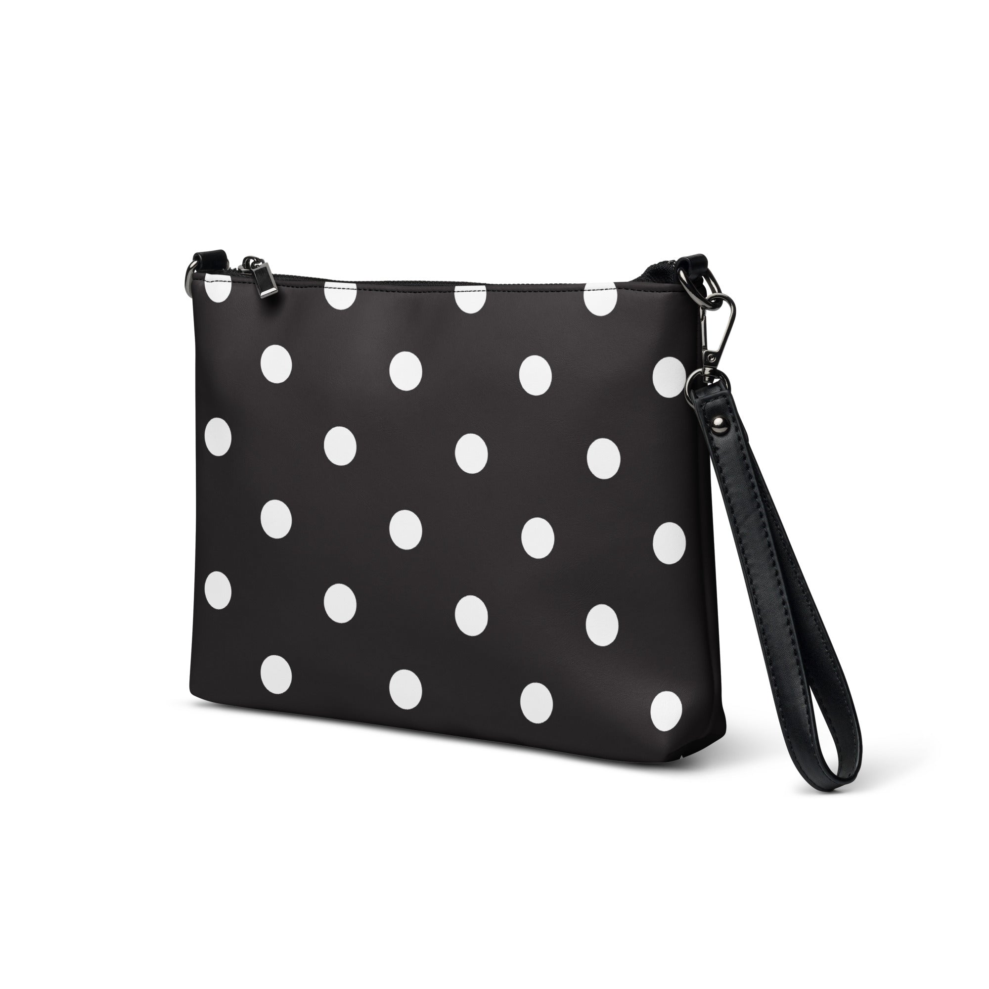 A black faux leather crossbody bag with white polka dots, featuring a zip-top closure and a detachable wrist strap.