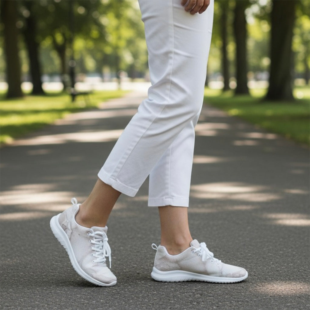Person wearing white marble pattern sneakers and pants walking on a path in a park.