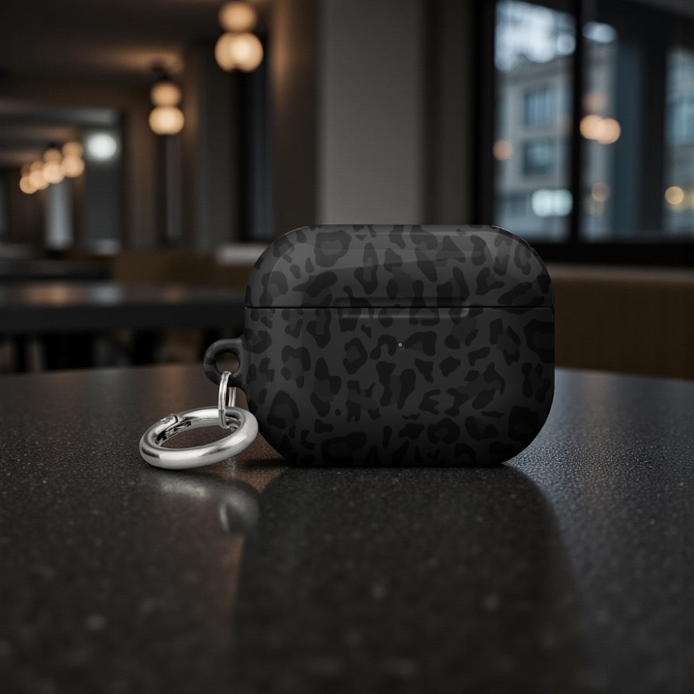 Black leopard print case with a keychain on a dark surface, blurred indoor background