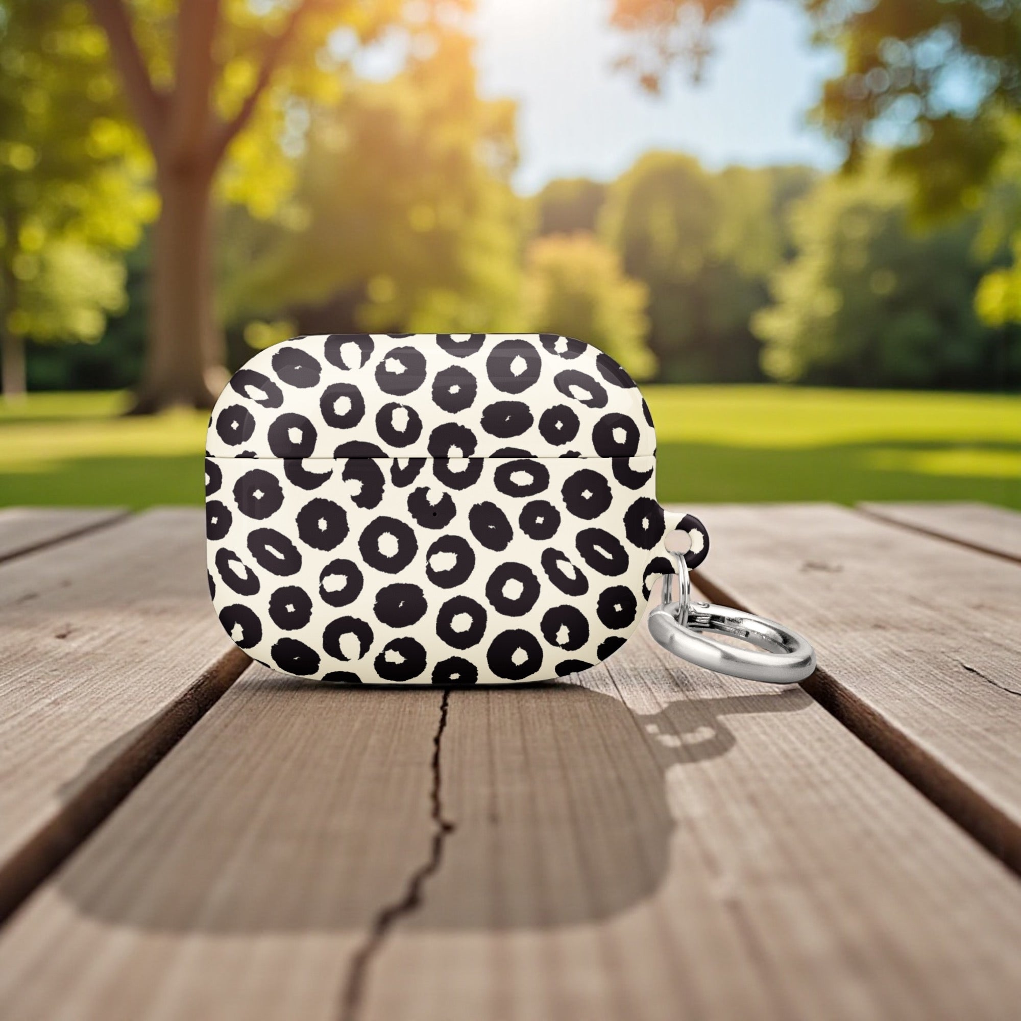 Black and white polka dot pouch with a keychain on a wooden surface in a park setting