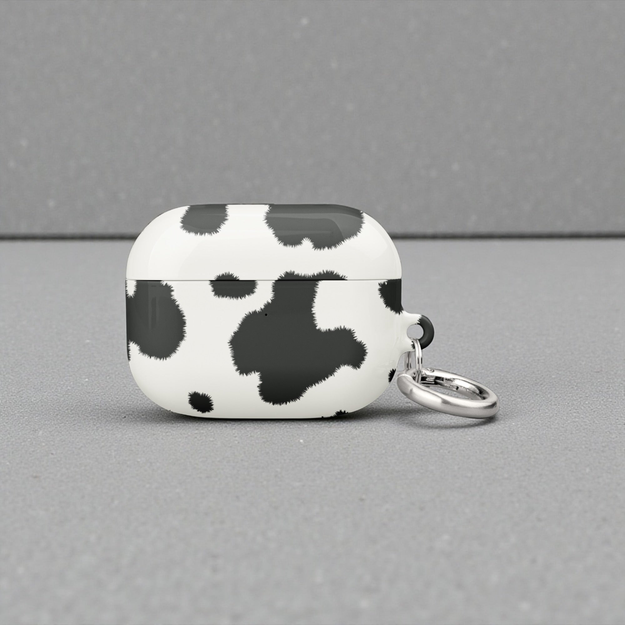 Cow print airpod case with a keychain on a gray background