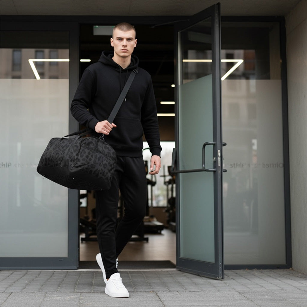 Man in black hoodie and pants holding a black duffel bag exiting a building.
